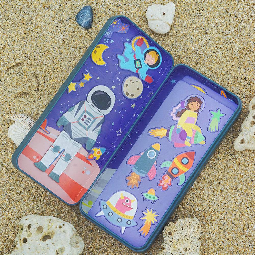 Die geöffnete Toydea Magnetspiel-Box zum Thema 'Weltraum' mit Astronauten und Raketen, die im Sand am Strand liegt.