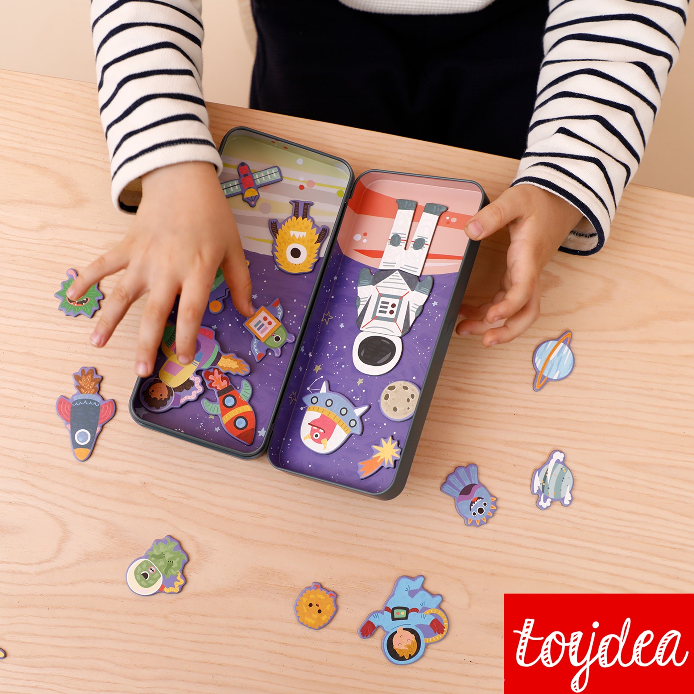 Nahaufnahme von Kinderhänden, die mit der Toydea 'Weltraum' Magnetspiel-Box auf einem Holztisch spielen.